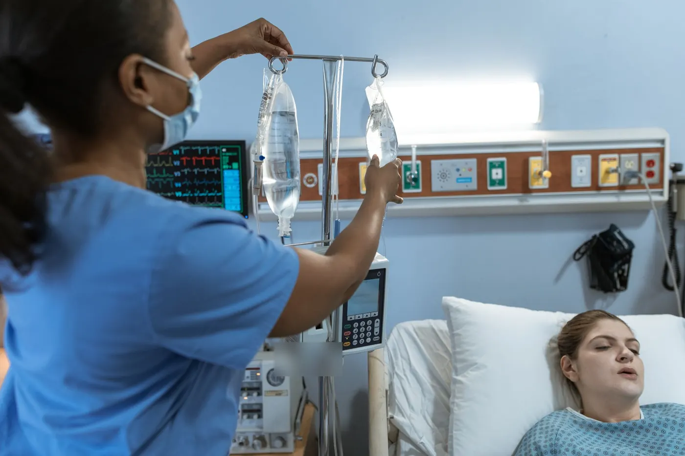 Nurse hanging IV bags above an infusion pump at a patient's bedside