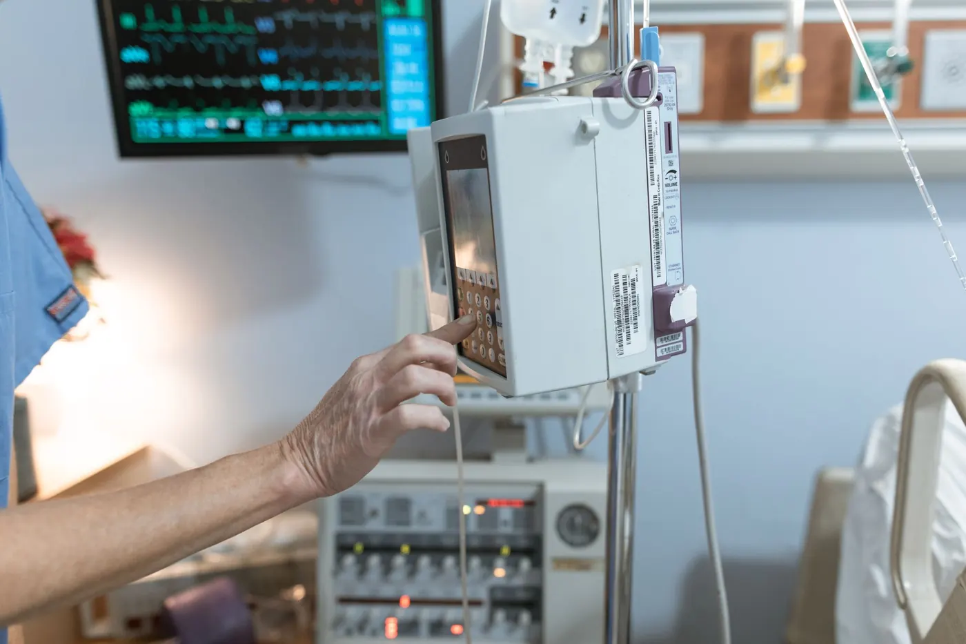Hand pressing the keypad of an infusion pump mounted on an IV pole