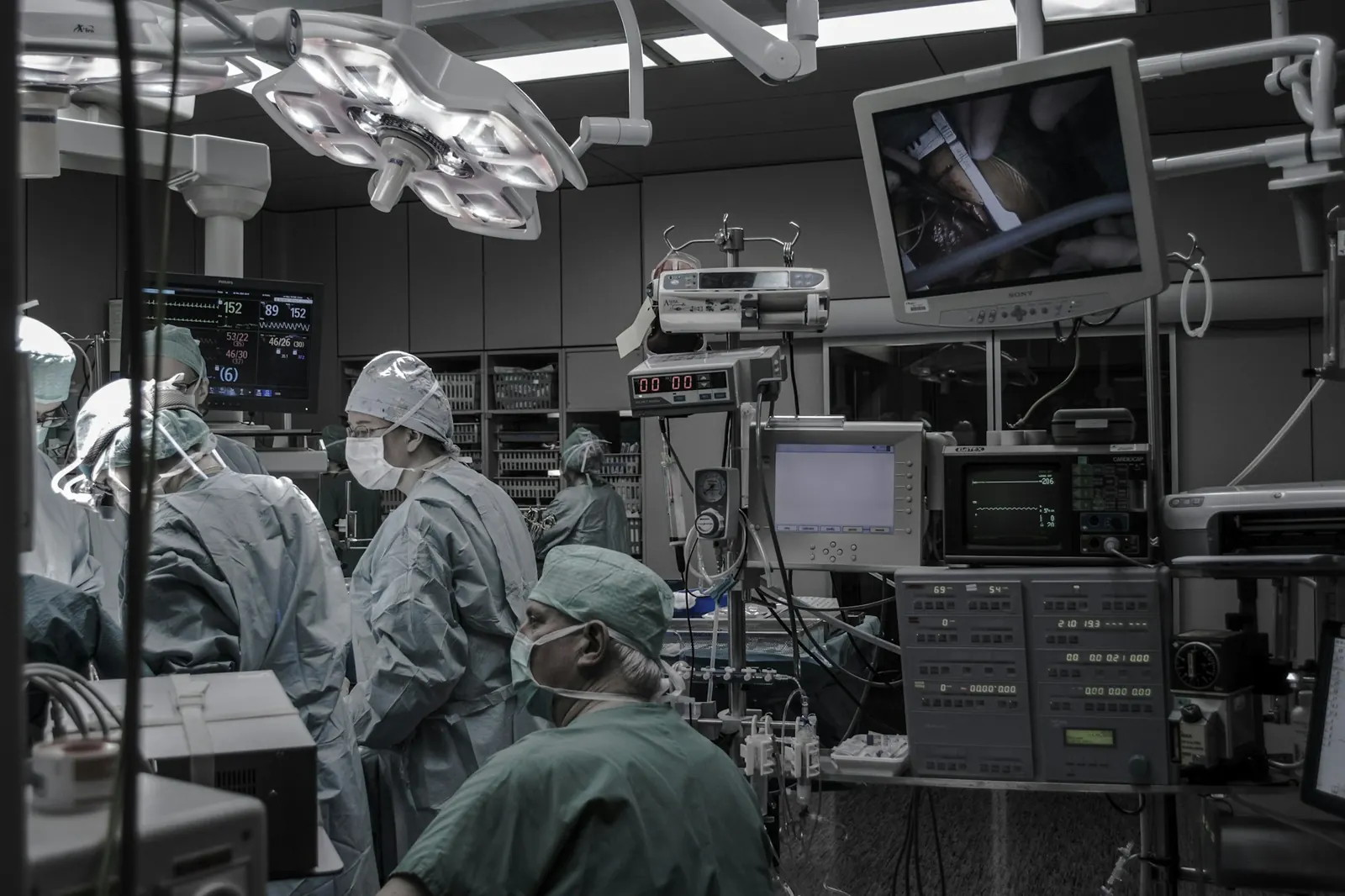 Surgical team at work in an operating room surrounded by monitors, pumps, and other medical equipment